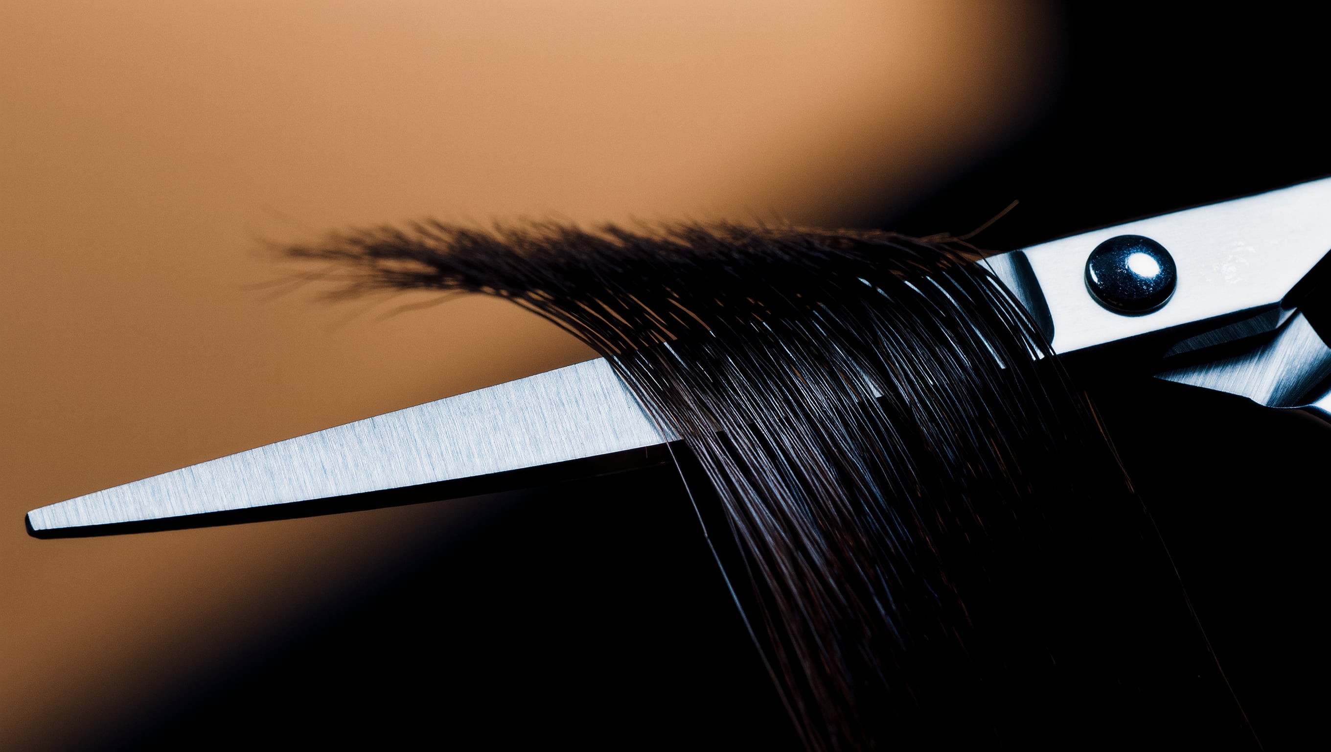 Eine geöffnete Friseurschere über einer gespannten Haarpartie, kaltes Licht auf der Klinge